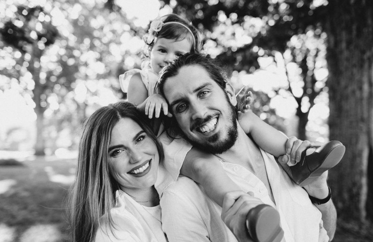 Black and white portrait of Josh and Rachael Lucas, a happy couple with their young child, smiling and embracing in a park setting, representing the personal and heartfelt wedding videography services of Lucas Studios NC.