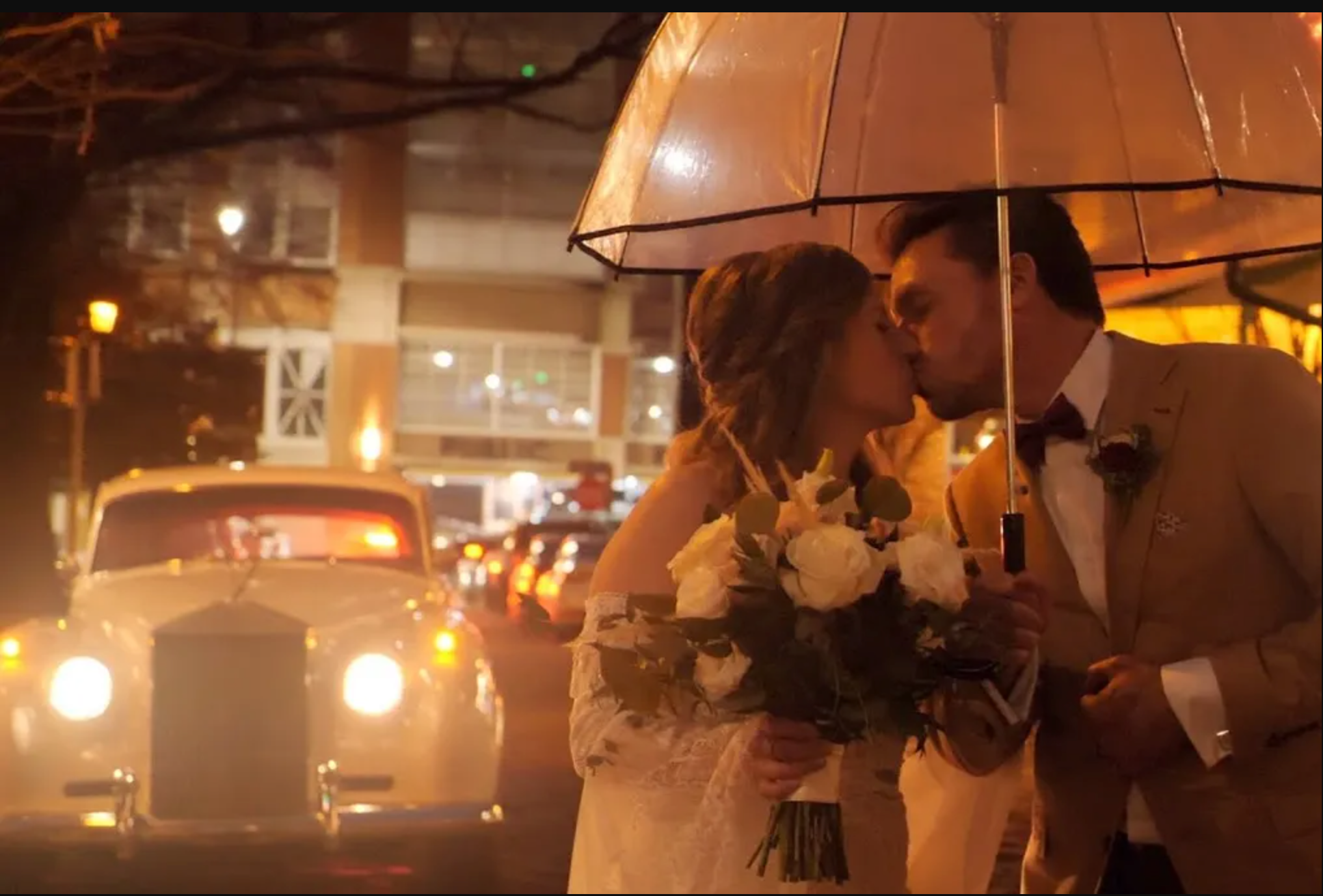 A couple sharing a tender kiss under an umbrella on a city street at night.